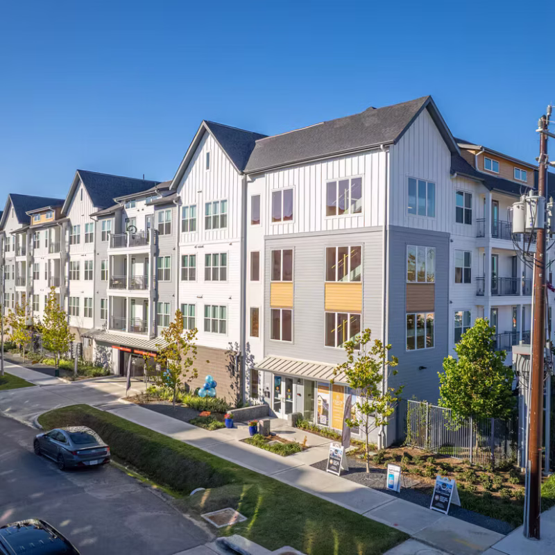 Four-story apartment building with ground-floor retail and awnings along a tree-lined street