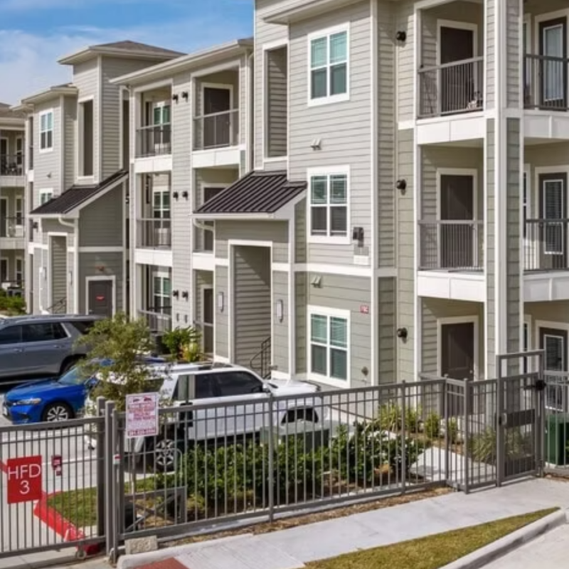 Three-story garden-style apartment building with balconies and mature landscaping