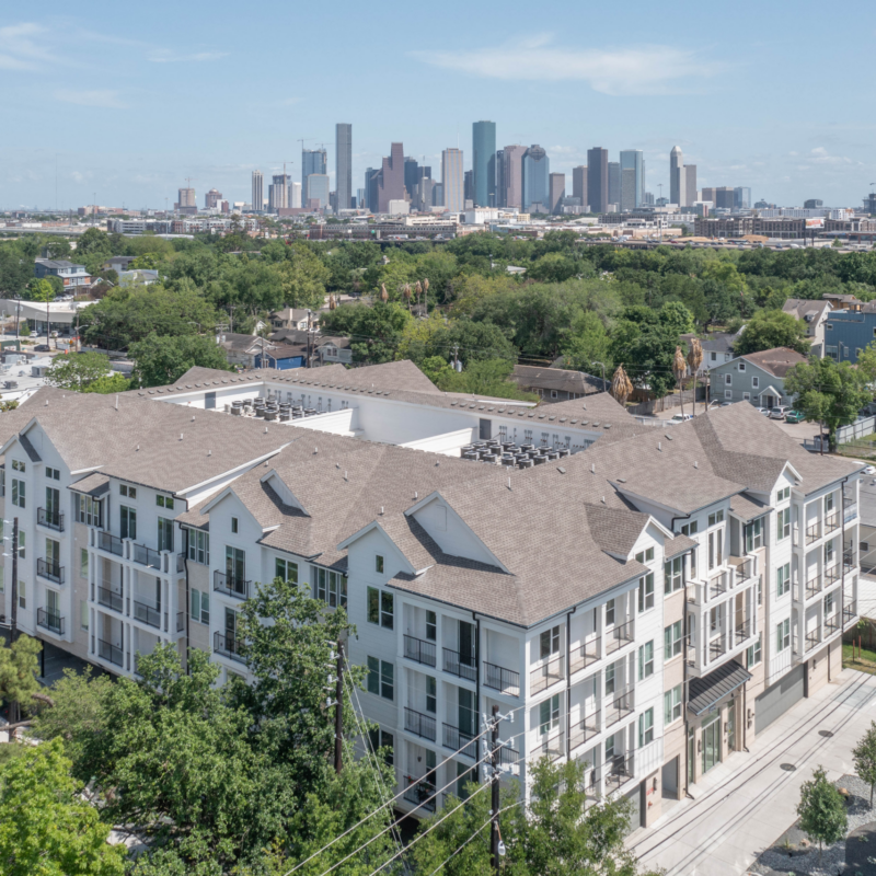 Aerial view of mid-rise apartments and townhomes with the Houston skyline beyond