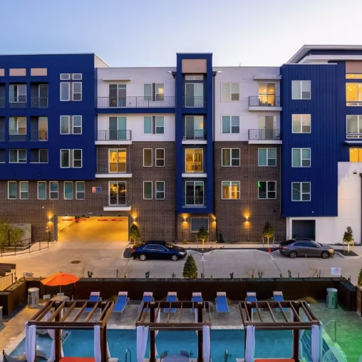 Five-story navy and white apartment building overlooking a courtyard pool at dusk