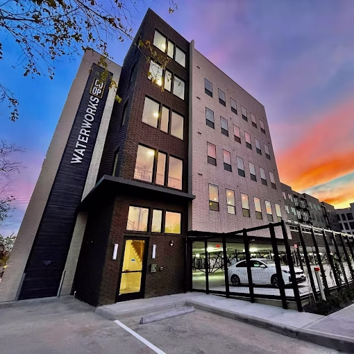 Brick mid-rise with Waterworks signage and a glass-walled parking level at sunset