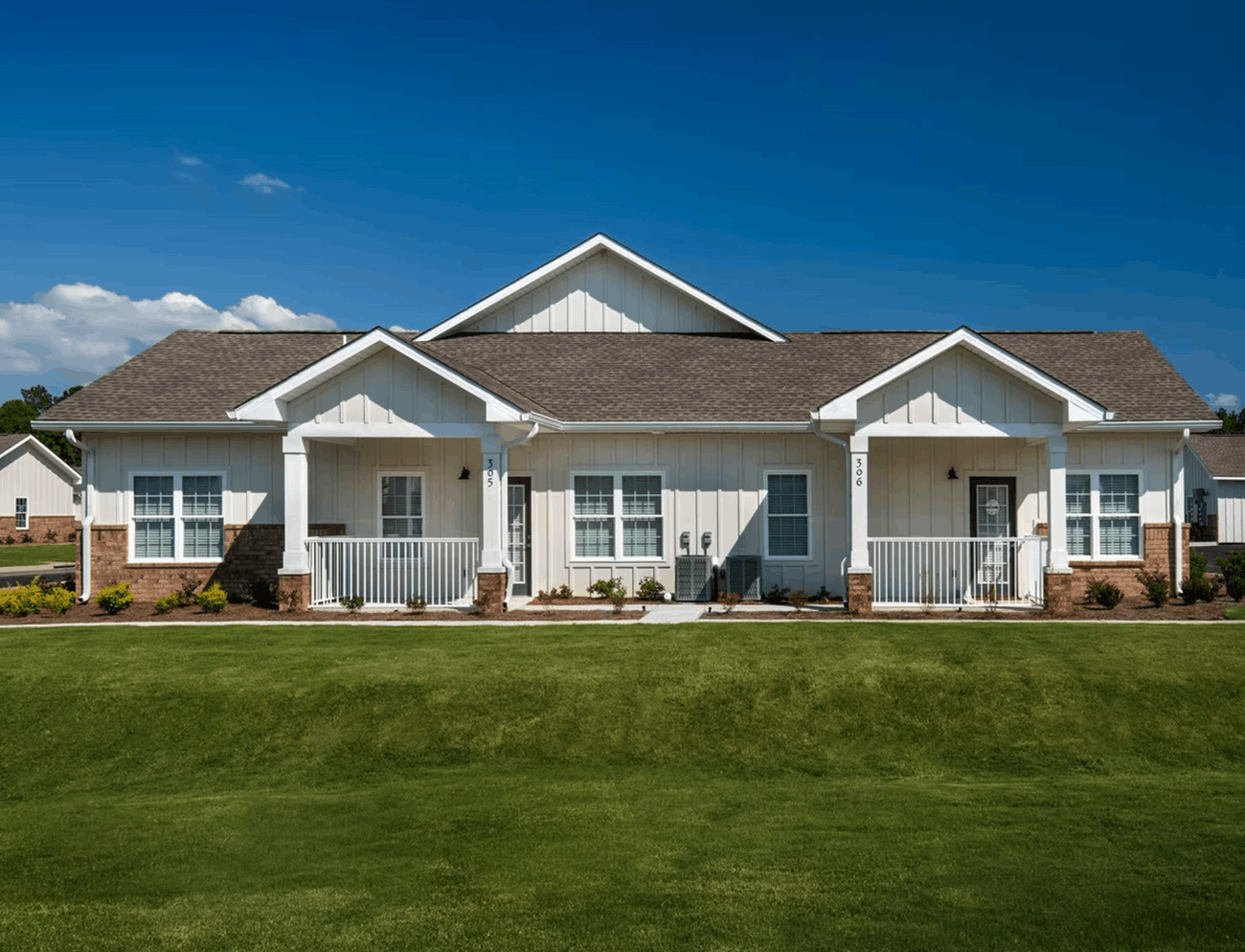 Single-story board-and-batten multifamily homes with covered porches and a landscaped lawn