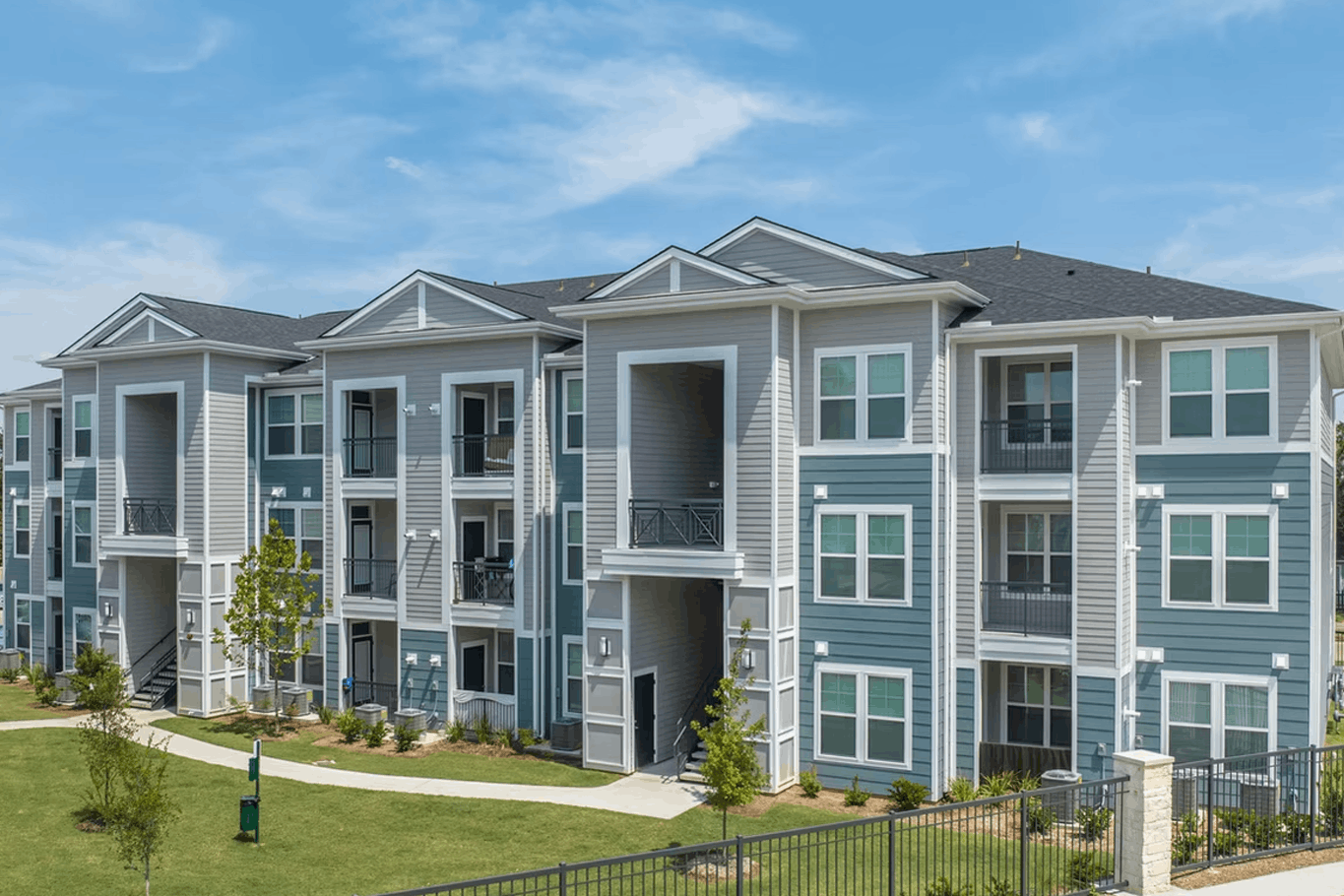 Three-story garden-style apartment building with balconies and mature landscaping
