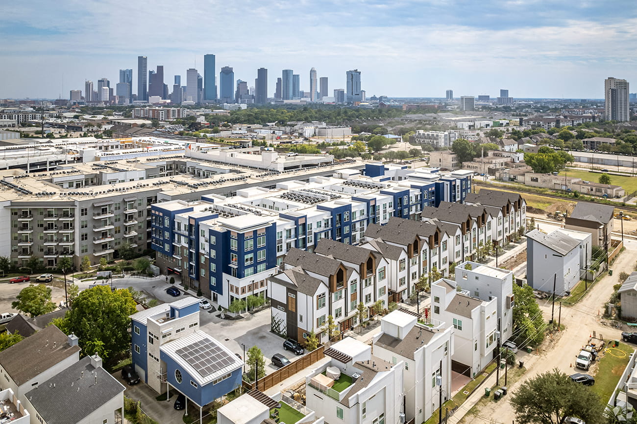 Aerial view of a mixed multifamily development of mid-rise apartments and townhomes with the downtown skyline beyond